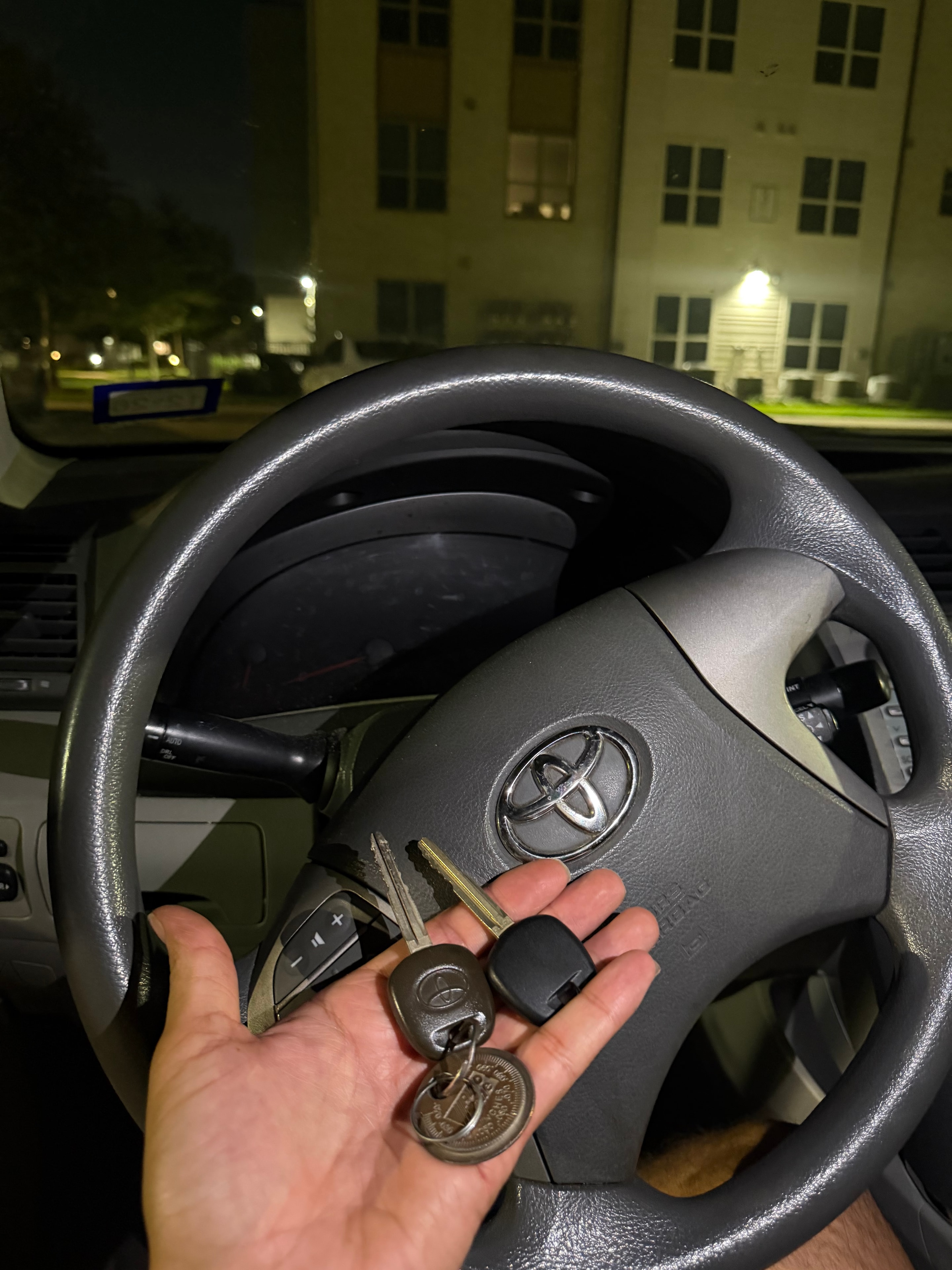 Hand holding Toyota car keys at steering wheel